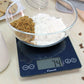 A lifestyle photo of an ARTI Digital Kitchen Scale weighing and surrounded by chocolate chip cookie ingredients.