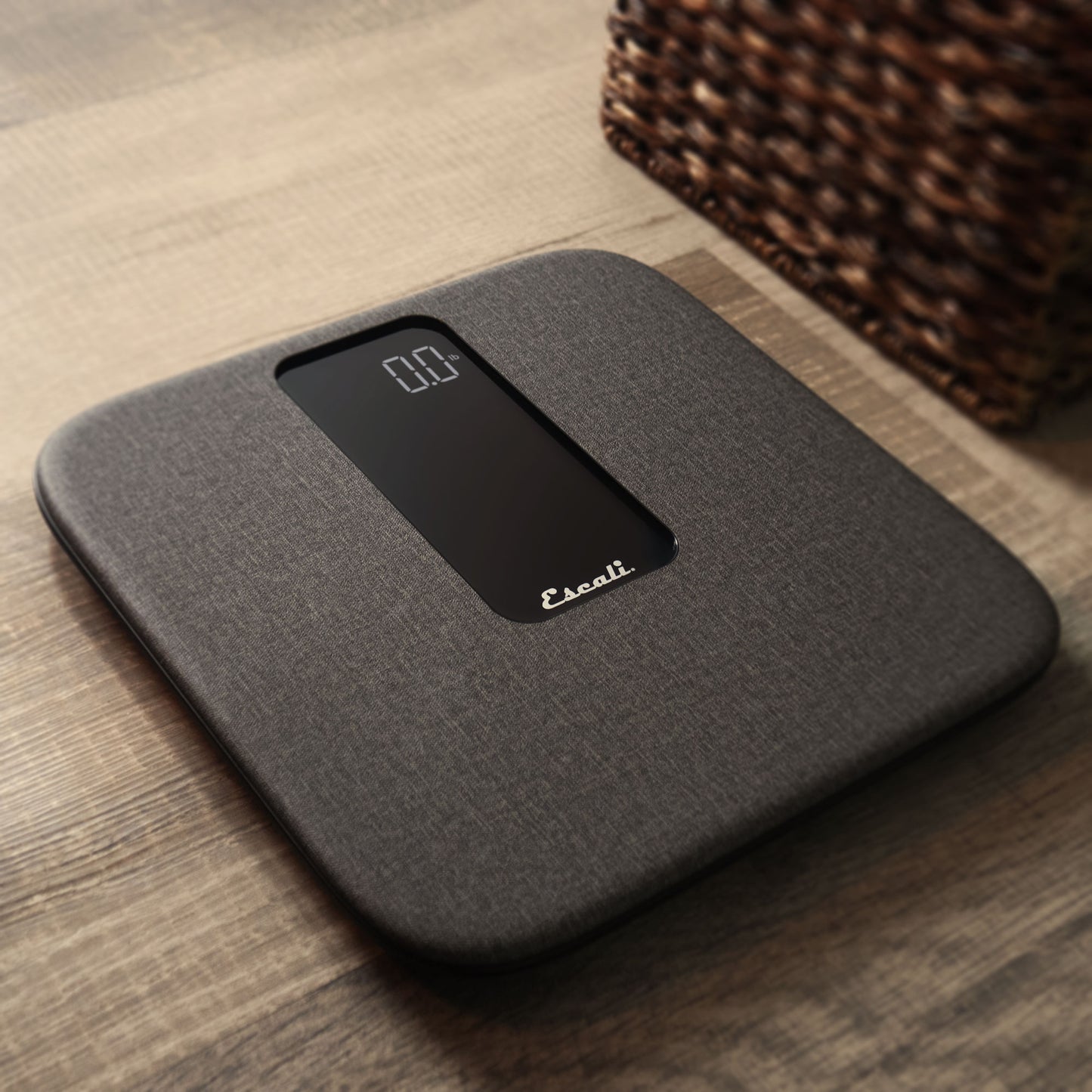 A lifestyle photo of the ComfortStep Bathroom Scale, sitting on a wood floor next to a basket.