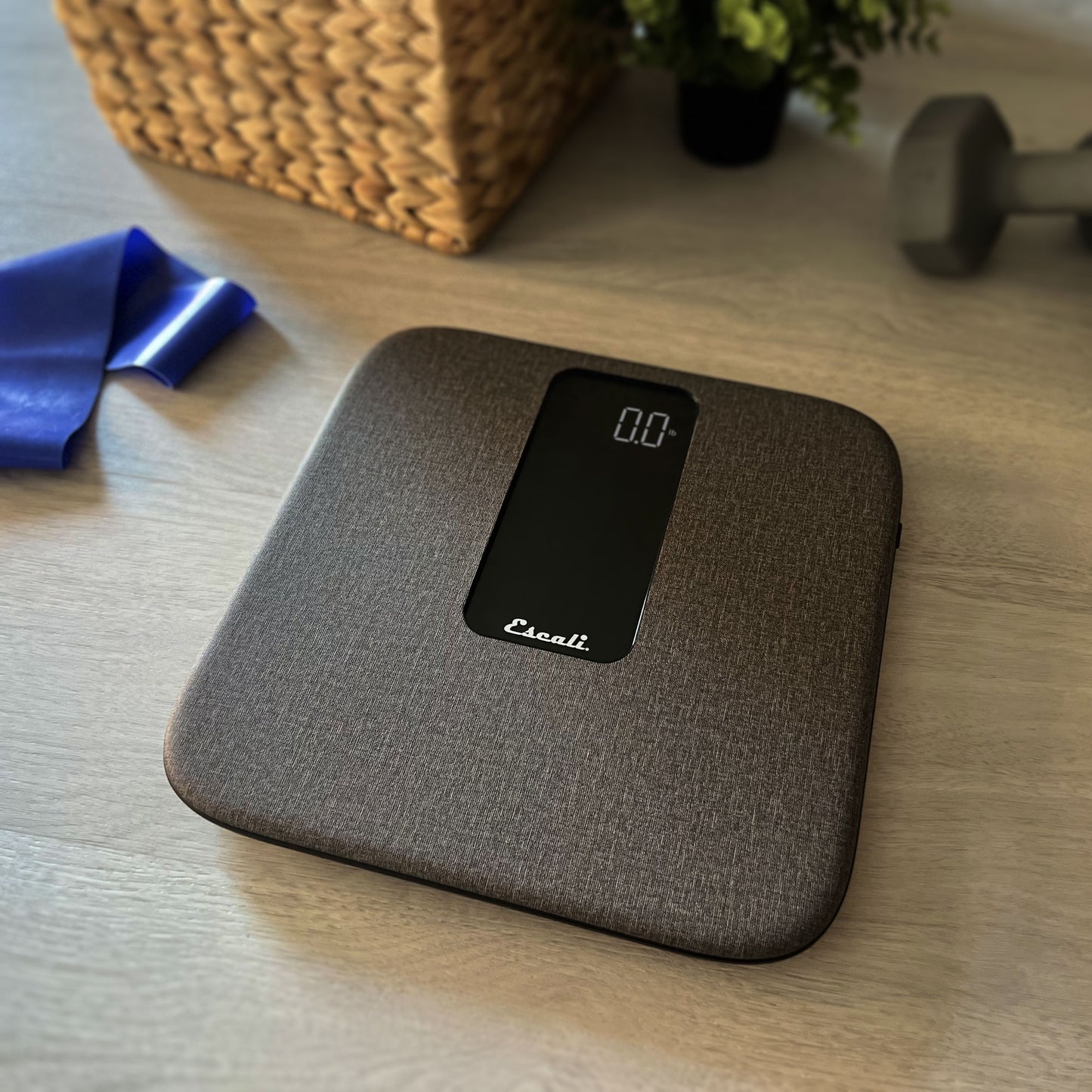 A lifestyle photo of the ComfortStep Bathroom Scale, sitting on a floor next to home gym equipment.