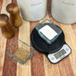 A lifestyle photo of a black Telero Digital Kitchen Scale sitting on a kitchen counter weighing sugar.