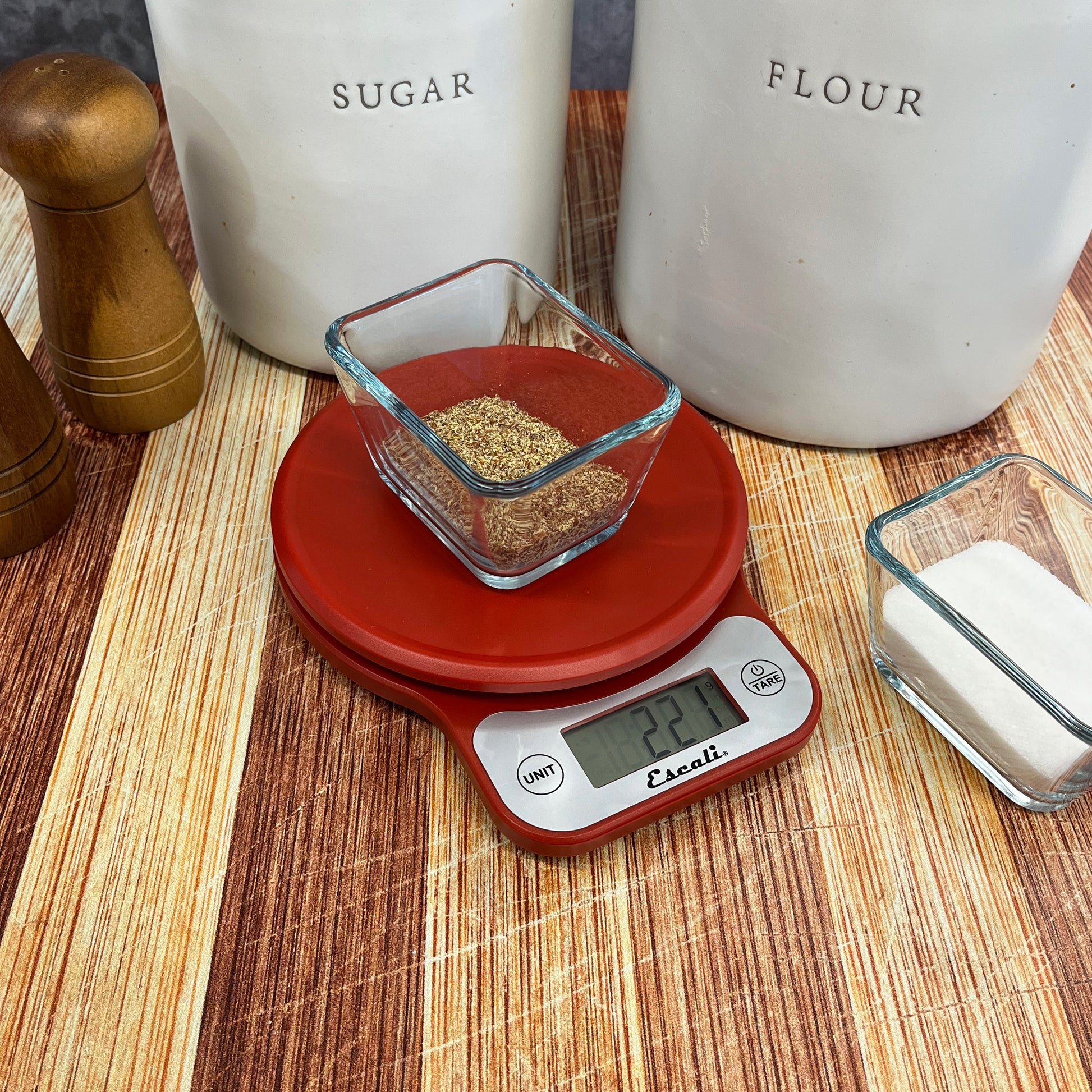 A lifestyle photo of a red Telero Digital Kitchen Scale sitting on a kitchen counter weighing flax seed. .