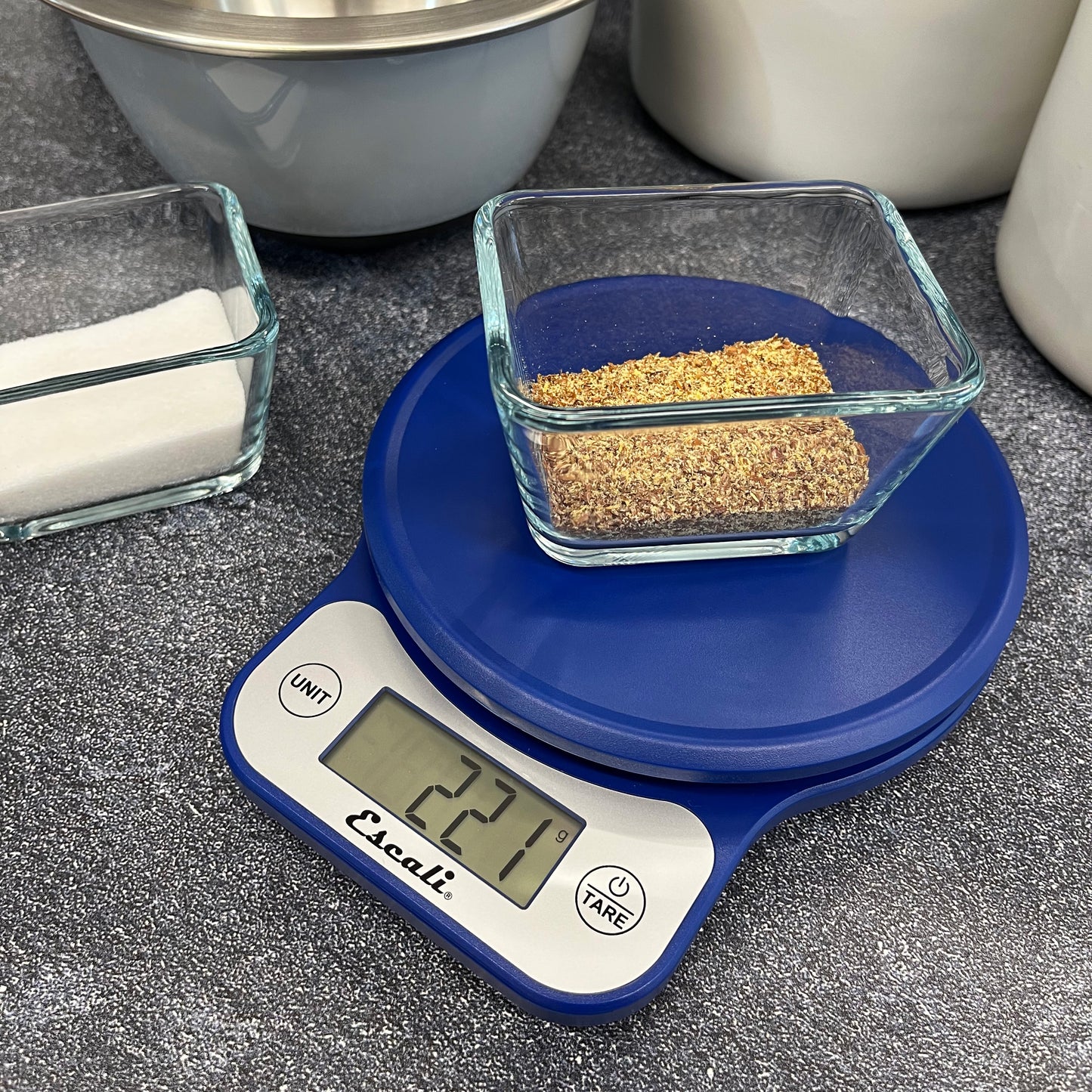 A lifestyle photo of a blue Telero Digital Kitchen Scale sitting on a kitchen counter weighing flax seed. .